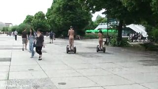 Two Girls Walk Naked Down The Street Riding A Skateboard